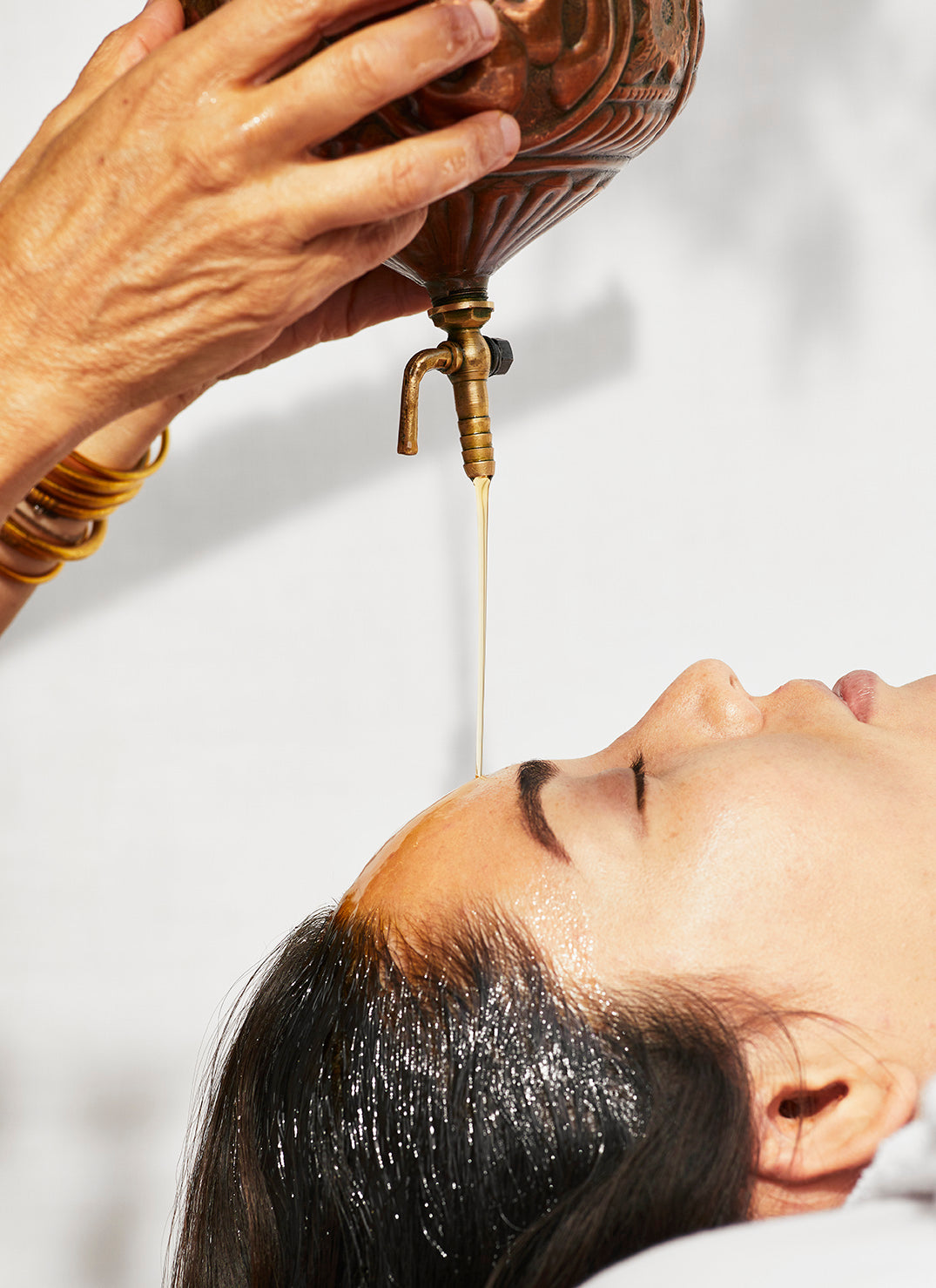 Woman lays with eyes closed as oil flows onto her forehead.